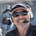 Smiling person in sunglasses and a headset, wearing a cap.