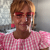 Person wearing red sunglasses and a pink checkered top, smiling indoors.