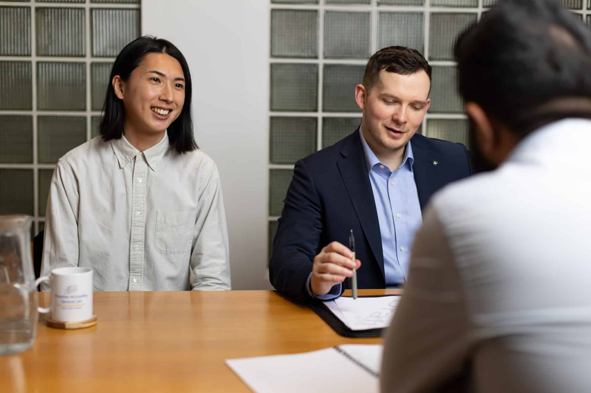 Three people engaged in a business meeting around a wooden table.